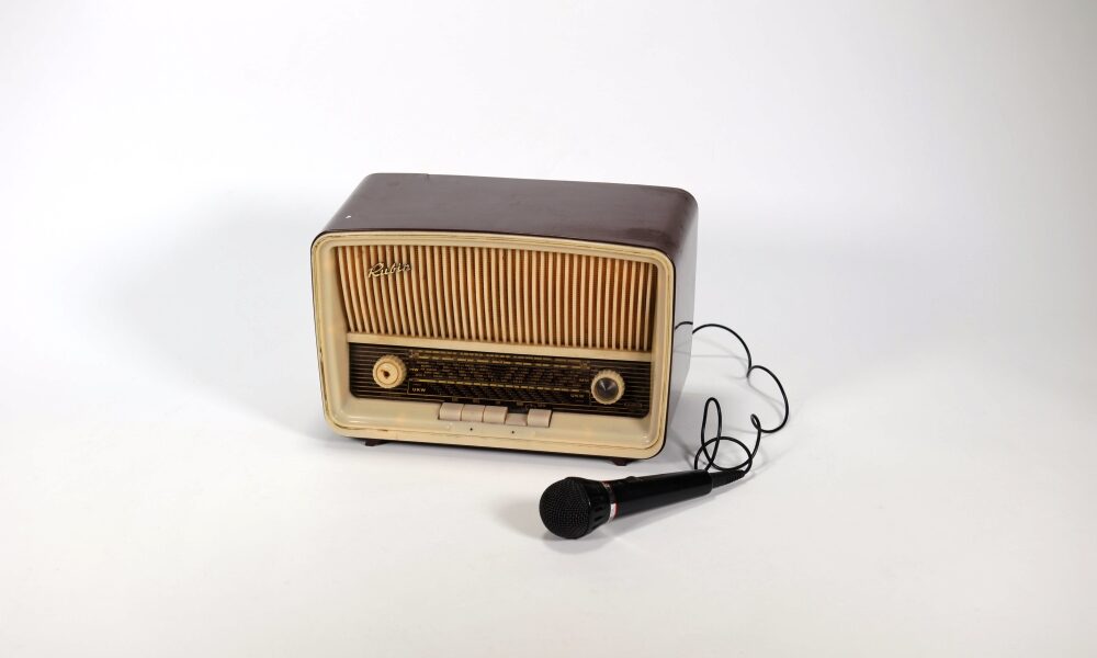 Ein altes Radio. Neben Radio liegt ein Mikrofon das durch ein Kabel mit dem Radio verbunden ist.